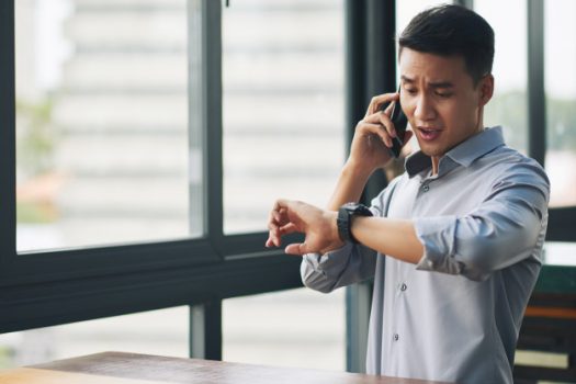 panicking-asian-man-talking-mobile-phone-looking-wristwatch_1098-17413